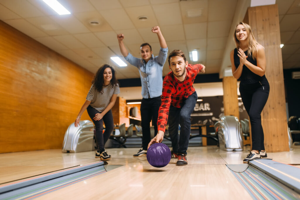 Bowler throws ball in lane with friends cheering behind him